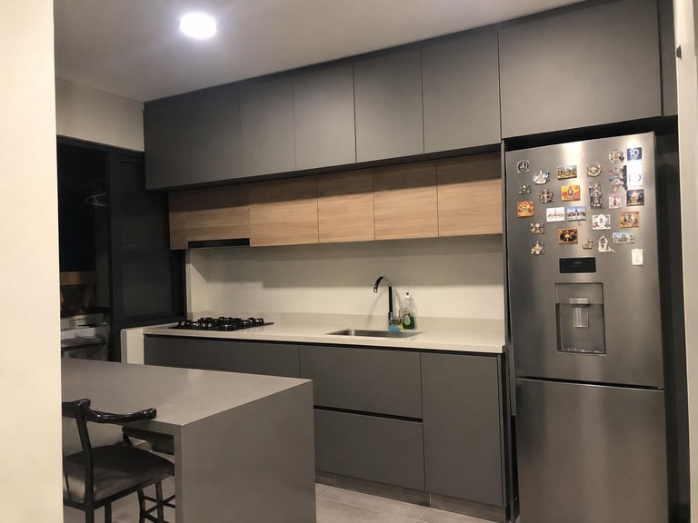 Modern kitchen with dark gray cabinetry, wood accents, stainless steel refrigerator, gas cooktop, white countertop island, and breakfast seating