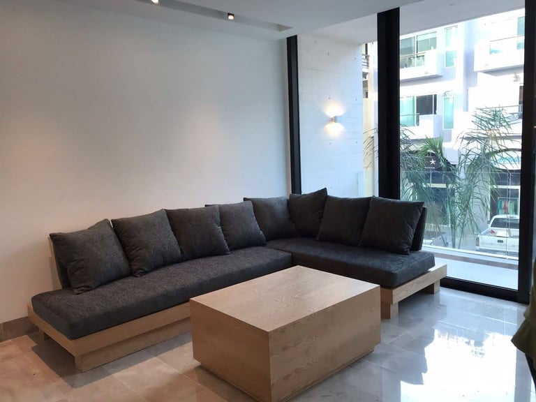 Modern living room with a dark gray L-shaped sectional sofa, wooden base, and a light wood coffee table on polished flooring near large windows