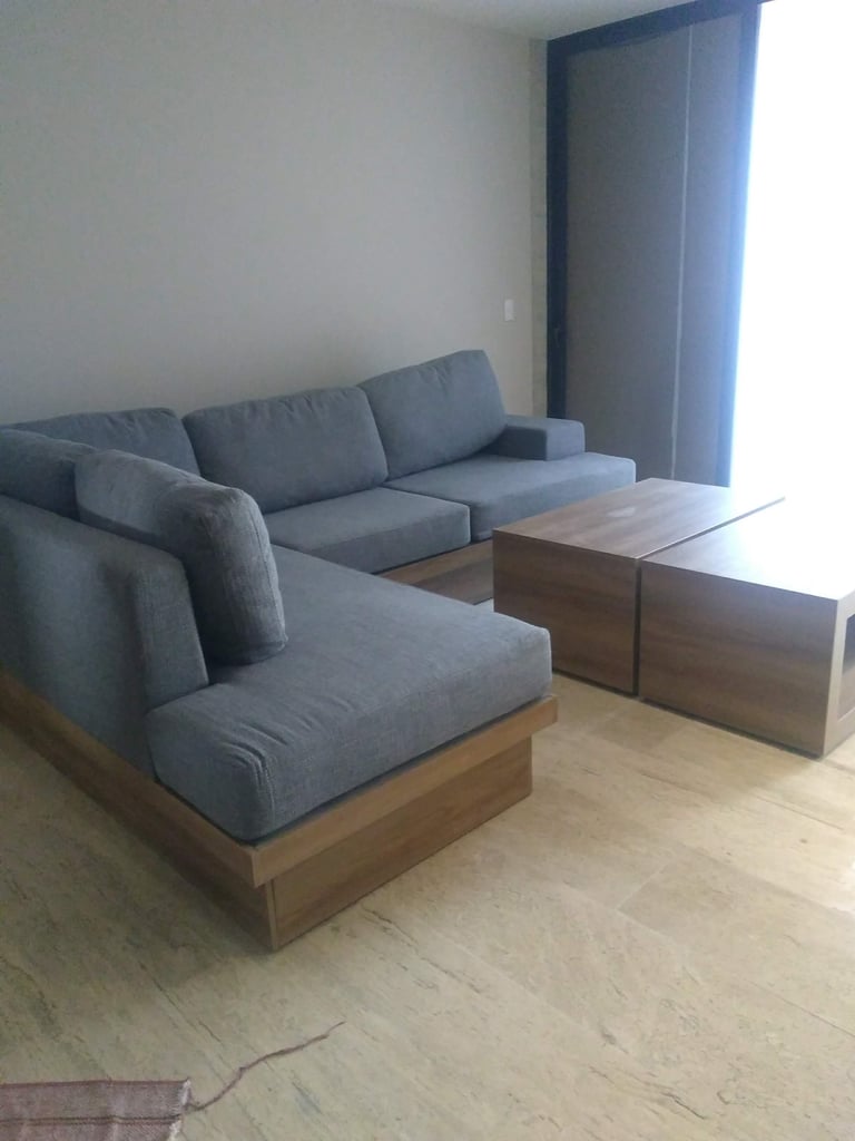 Modern living room with gray modular sectional sofa with wooden base, wooden coffee table, and large window with blue curtains