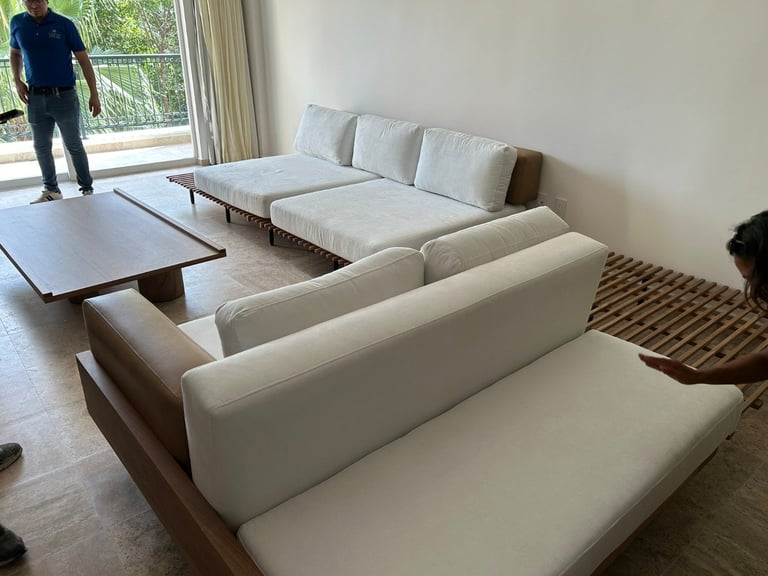 Modern living room with a large L-shaped white sectional sofa, low wooden table, and a person standing by the window